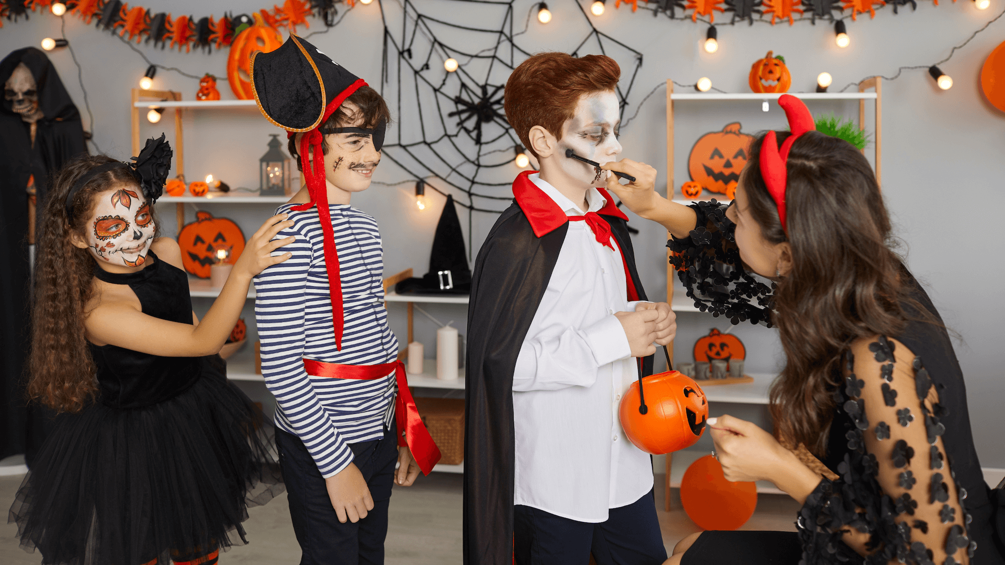 young boy at halloween party getting his face painted with white and black face paint with little boy and girl behind him watching