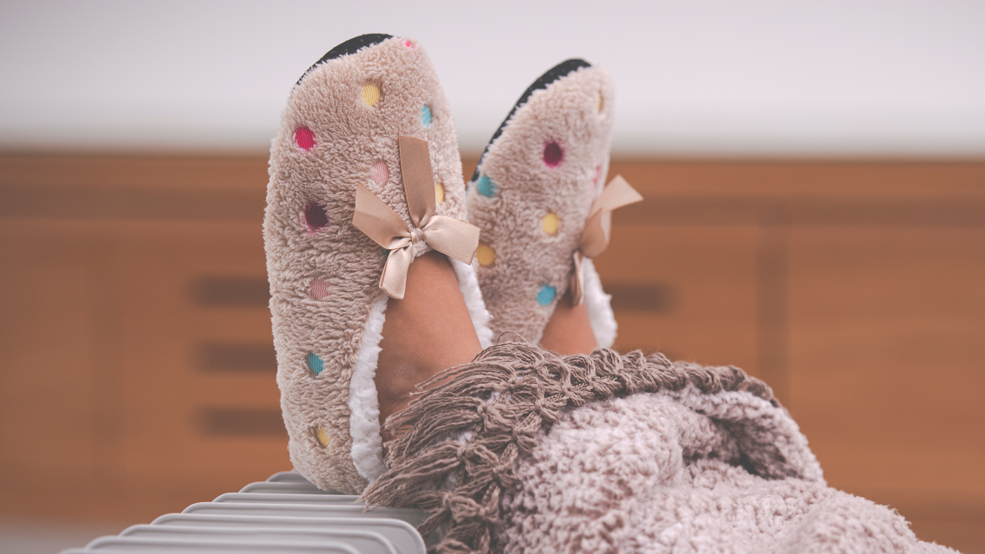 little girls slippers with multi colour polka dots on a heater with a blanket over legs