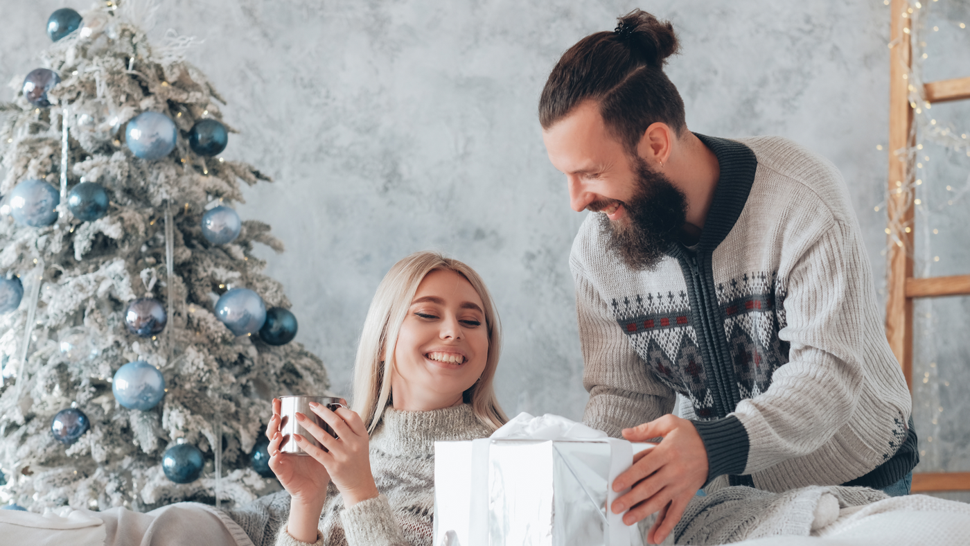 couple on christmas day in front of tree opening large gift box and smiling