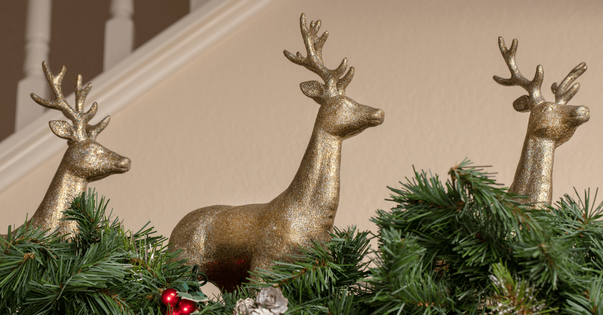 3 gold ornamental reindeer decorations on green garland with berry accessories