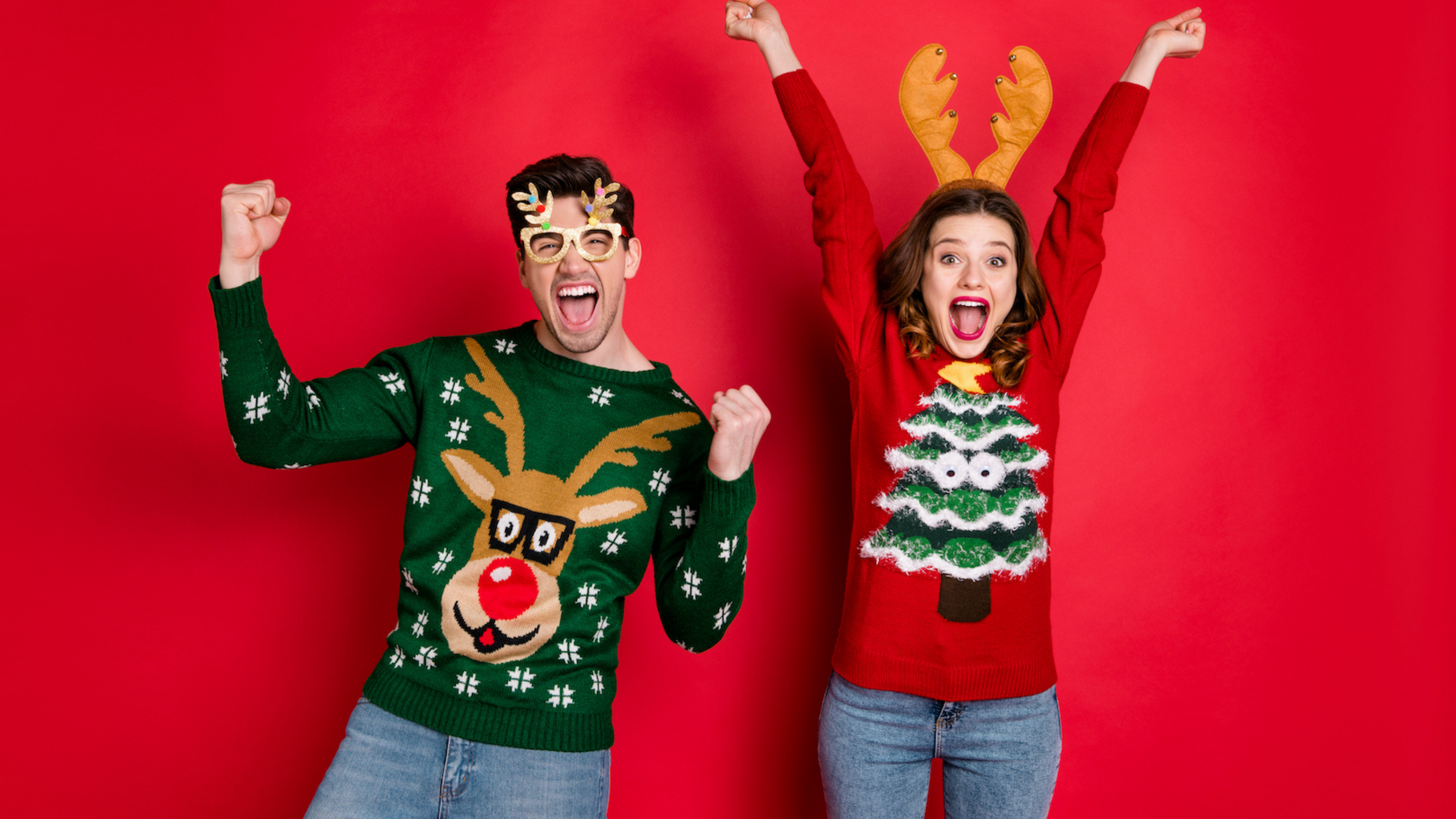 boy and girl wearing christmas jumpers and jumping for joy