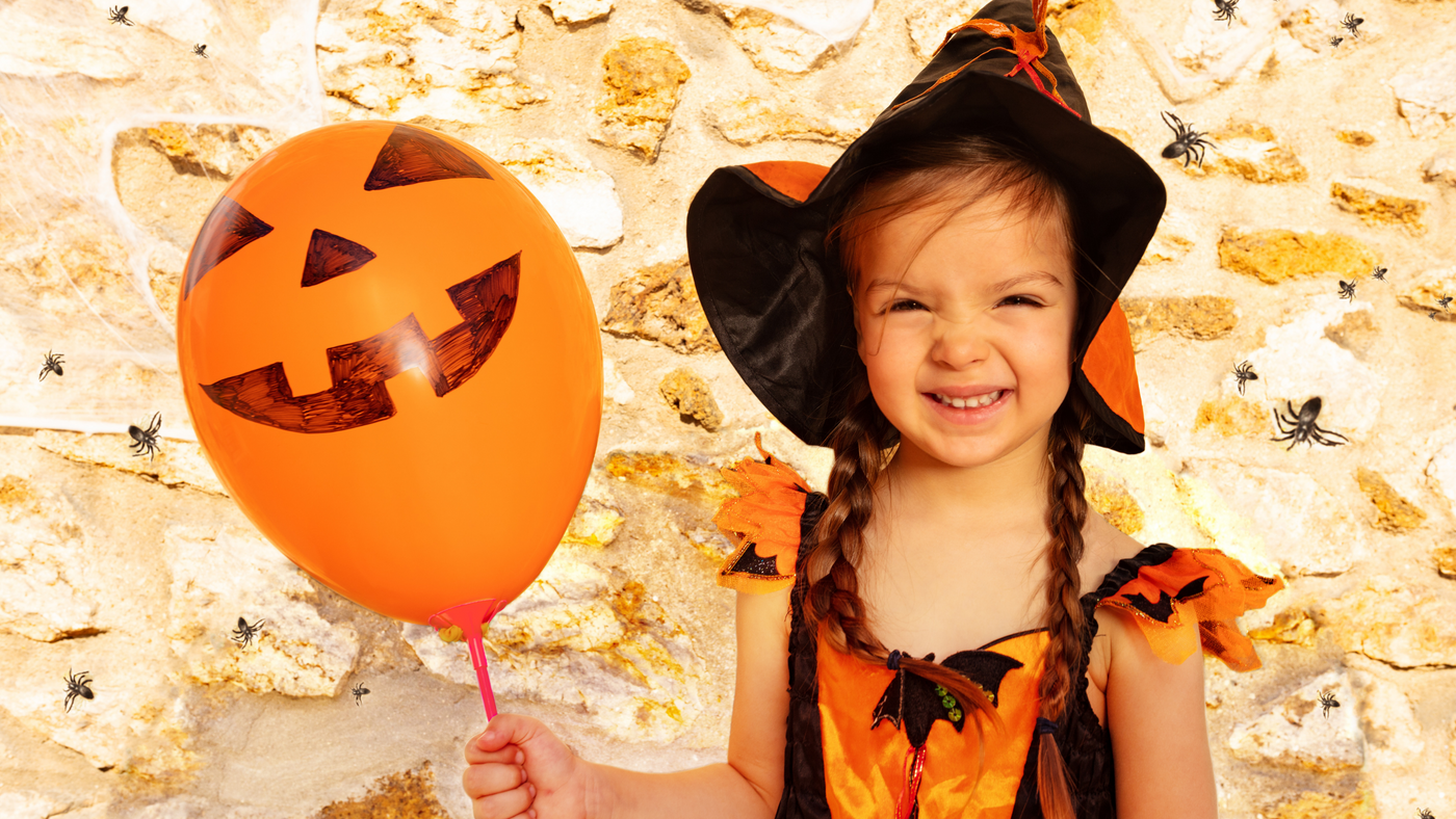 little girl wearing orange and black witch costume and holding a pumpkin balloon