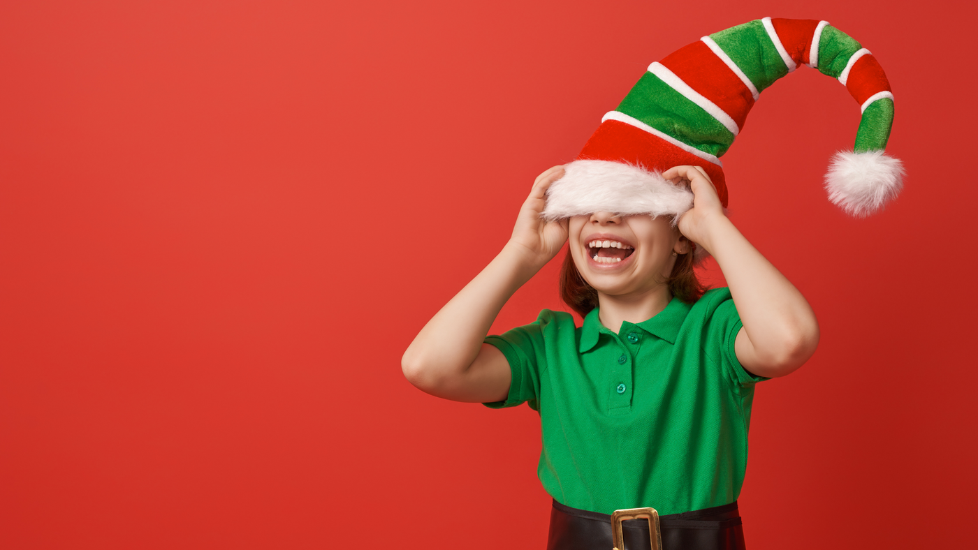 little girl wearing a large elf hat and laughing as it falls over her eyes