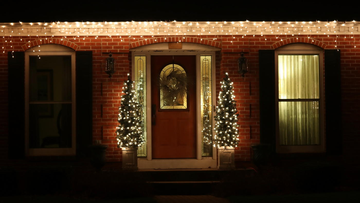 front of house with icicle lights and pre-lit topiary trees beside the door