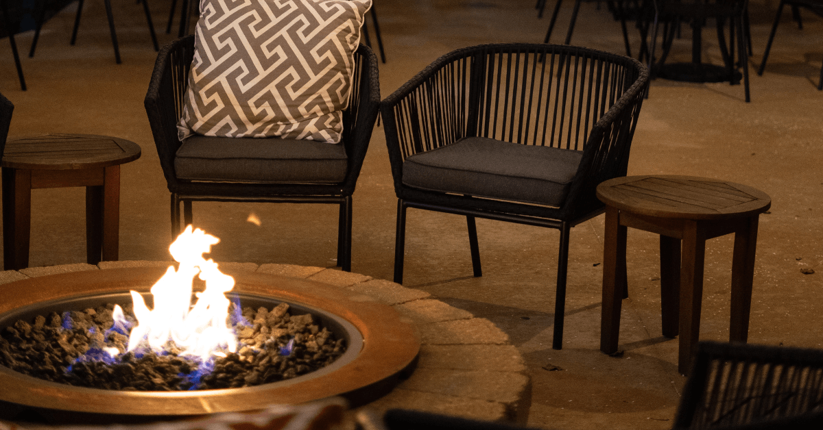 fire pit with flames in front of string chair furniture at night patio