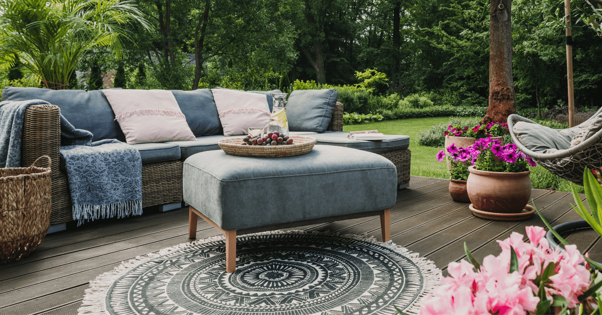 grey rattan sofa set on wooden patio space with plush greey ottoman and pink coloured flowers in the foreground