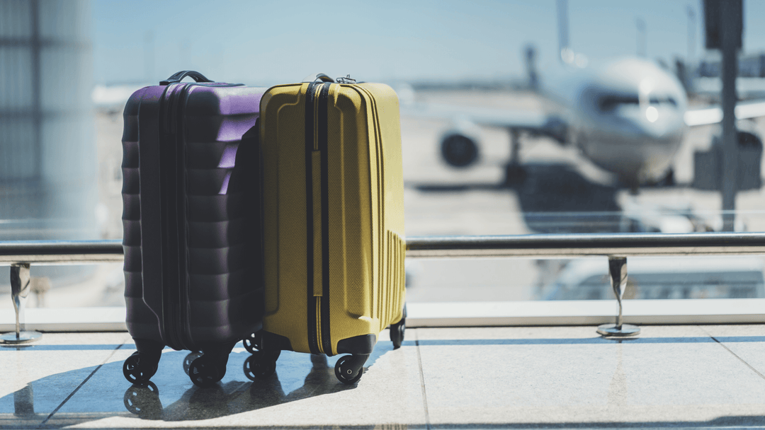 purple and yellow suitcase on airport in front of airport window with airplane visible in background