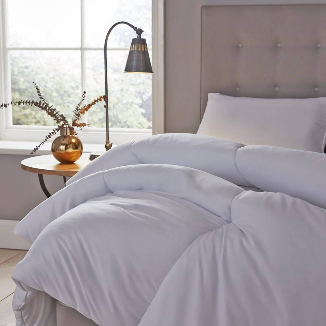 white quilt on a bed with side table and lamp