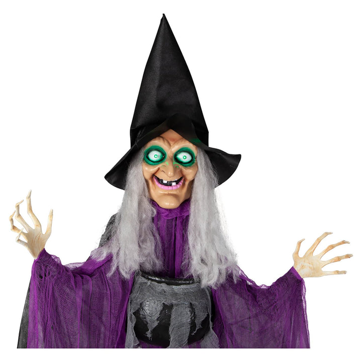 Close up of witch figure with light up green eyes purple cloak and black cauldron