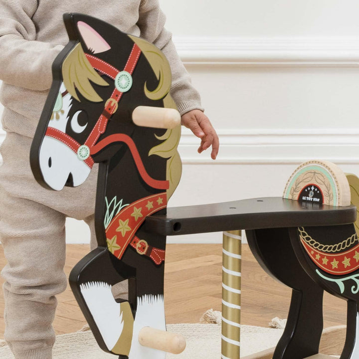 Child playing with a wooden rocking horse toy indoors