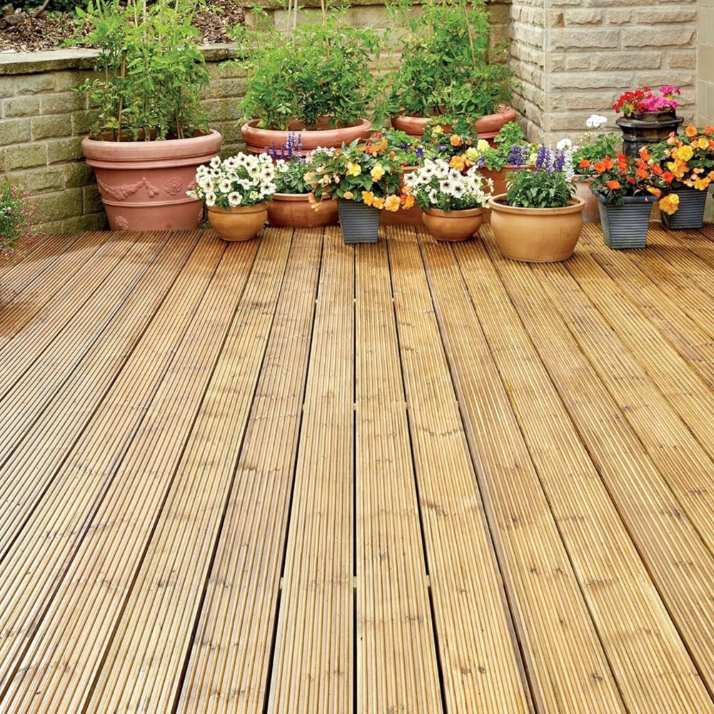 Row of potted plants on a wooden deck with a stone wall in the background
