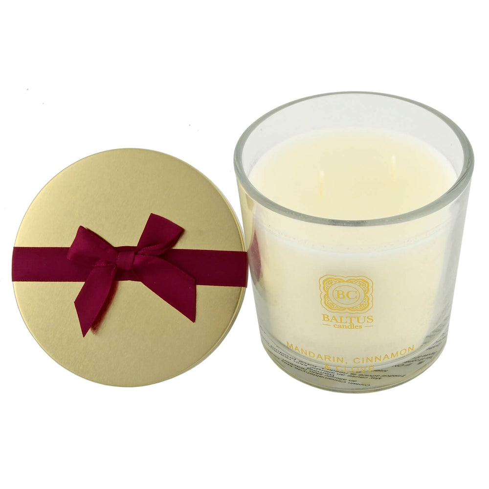 Glass candle with a red ribbon next to a round gold lid on a white background