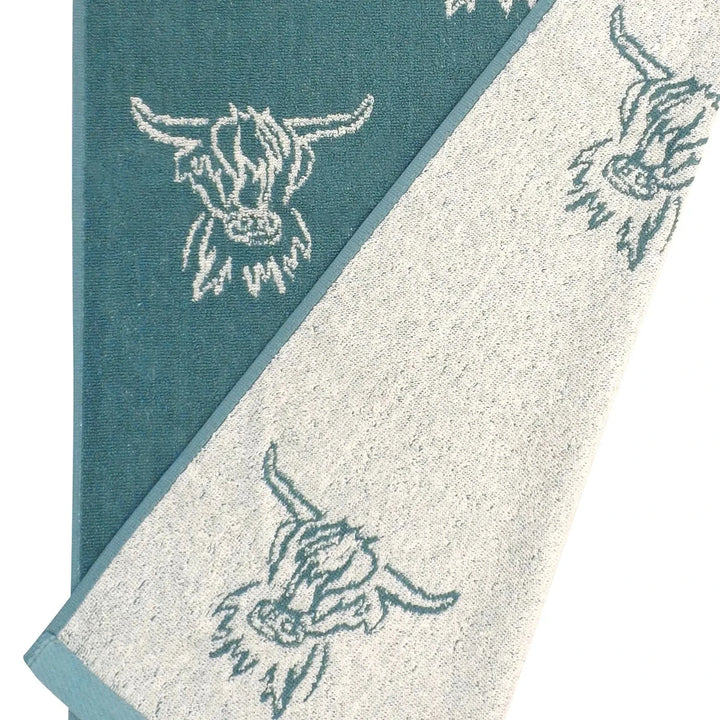 Close up of a highland cow pattern tea towel with green and beige reversible design