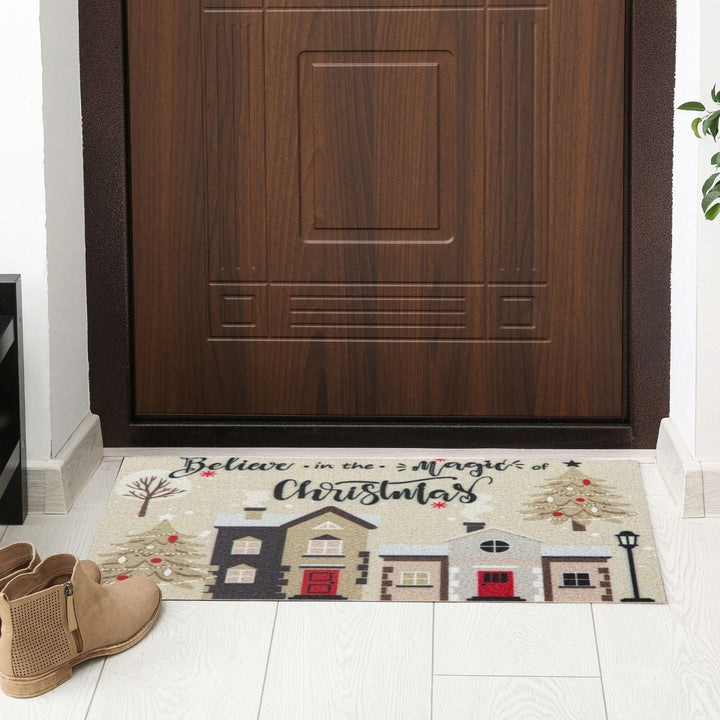 Christmas-themed doormat with houses and text in front of a wooden door.