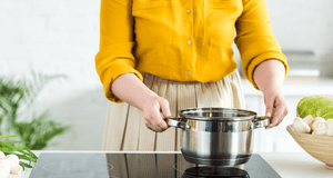 close up of lady holding a silver stainless steel stock pot over black oven hob