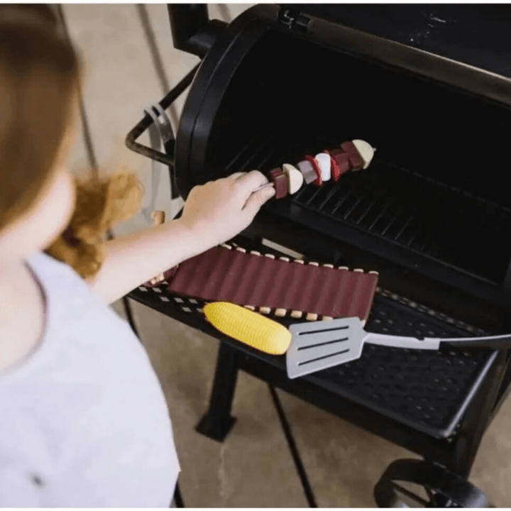 top view of little girl adding pretend skewer, honey ribs and corn on the cob toy food onto toy grill chamber