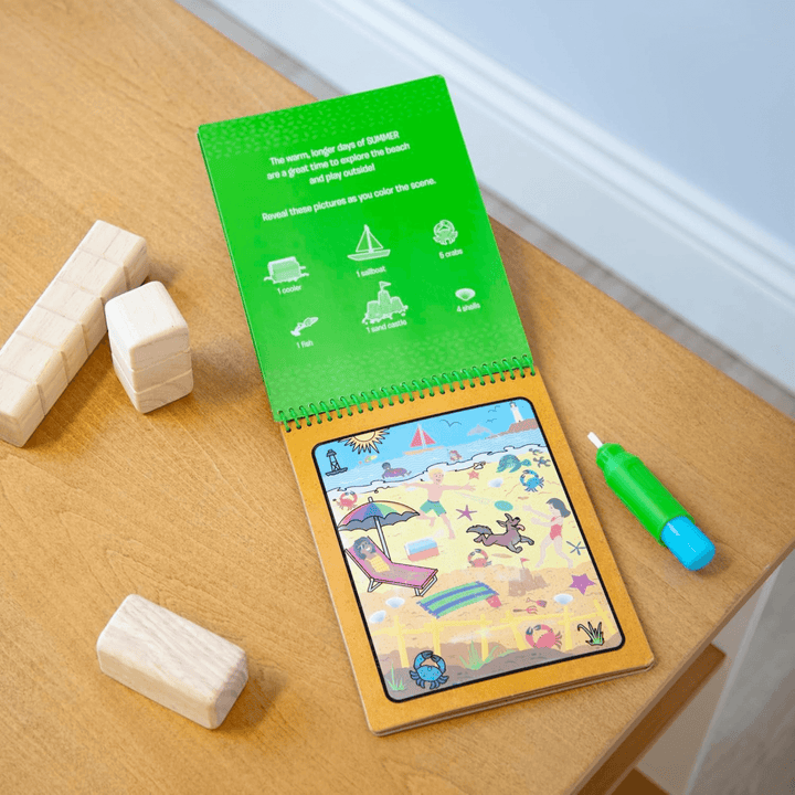 water reveal activity book on wooden table top with sumer scene fully completed with water pen to the side