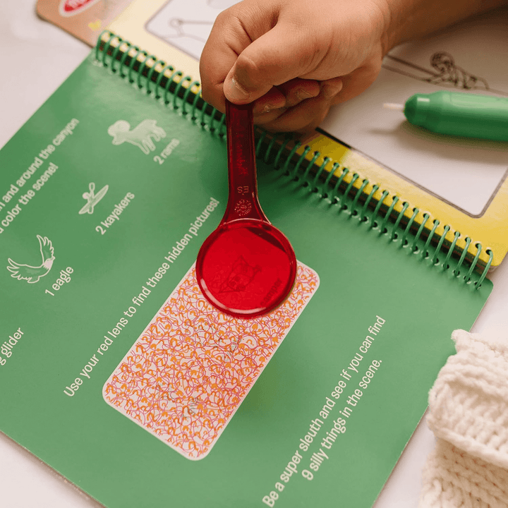 little hand holds red magnifying lens above hidden picture panel to reveal additional puzzles