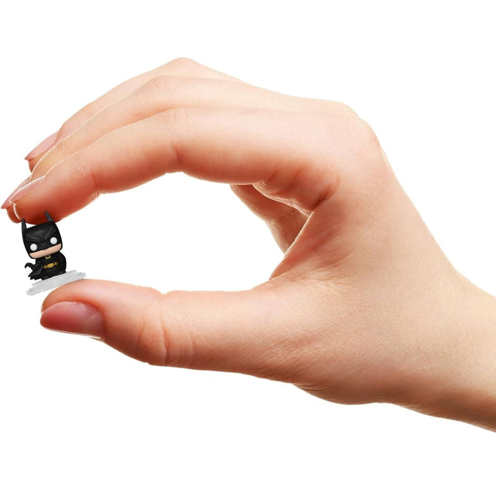 Hand holding a small black batman figurine on a white background