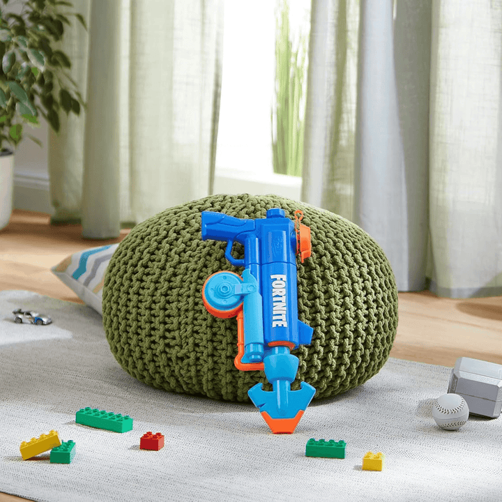 blue and orange super soaker leaning in footstool in living room beside building blocks and toy cars