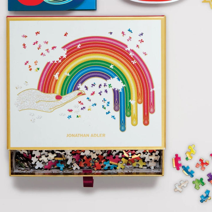 jonathan adler rainbow shaped puzzle in box with cold edging and pull out drawer on desk top with small pieces to the side