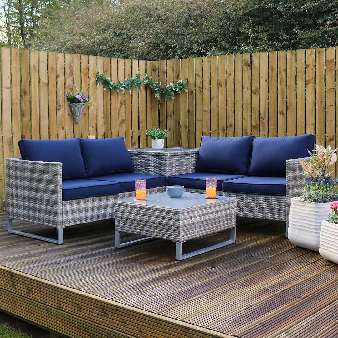 treviso sofa set on a wooden decking space outdoors, grey rattan material with chunky thick blue cushions, planters to the side, with drinks and snacks resting on table top