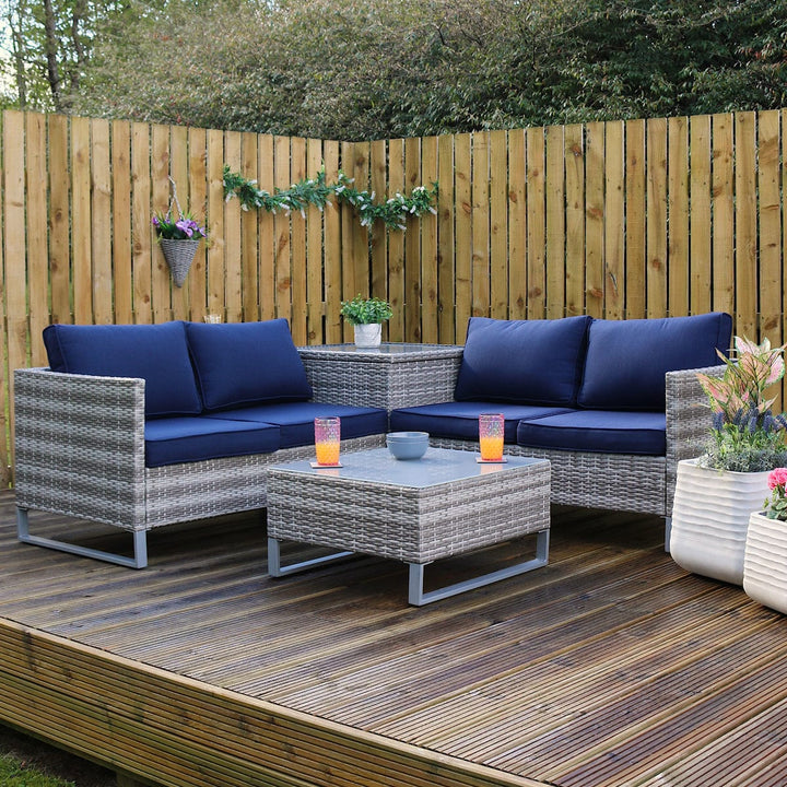 treviso sofa set on a wooden decking space outdoors, grey rattan material with chunky thick blue cushions, planters to the side, with drinks and snacks resting on table top