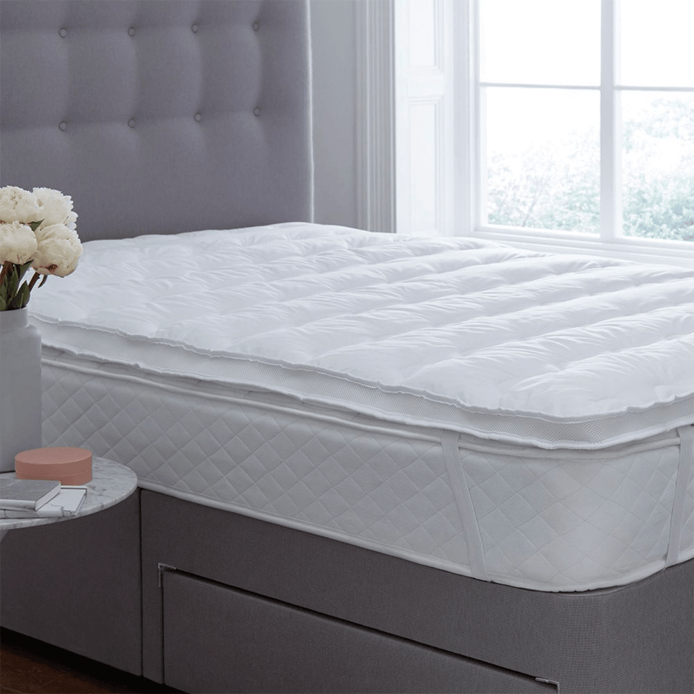 White mattress topper on a bed in a bedroom with a window in the background