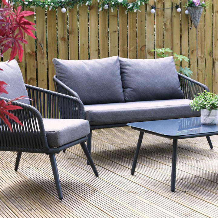close up of teramo sofa set with grey chunky cushions on wooden decking space with wooden fence in the background, planter and red tree