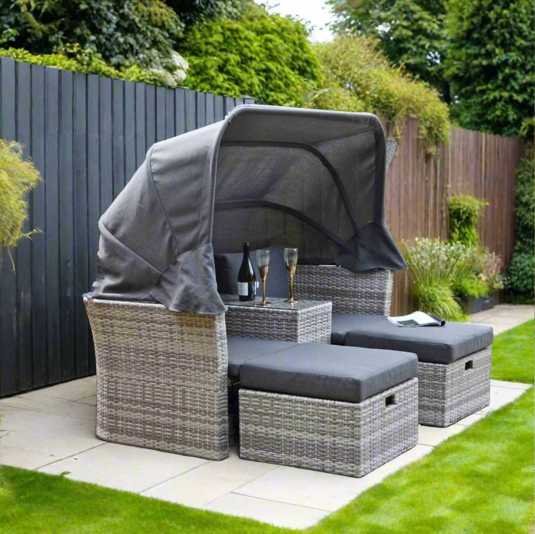 arezzo canopy day bed sofa set on patio space in front of grey coloured fence with bushes and trees in the background