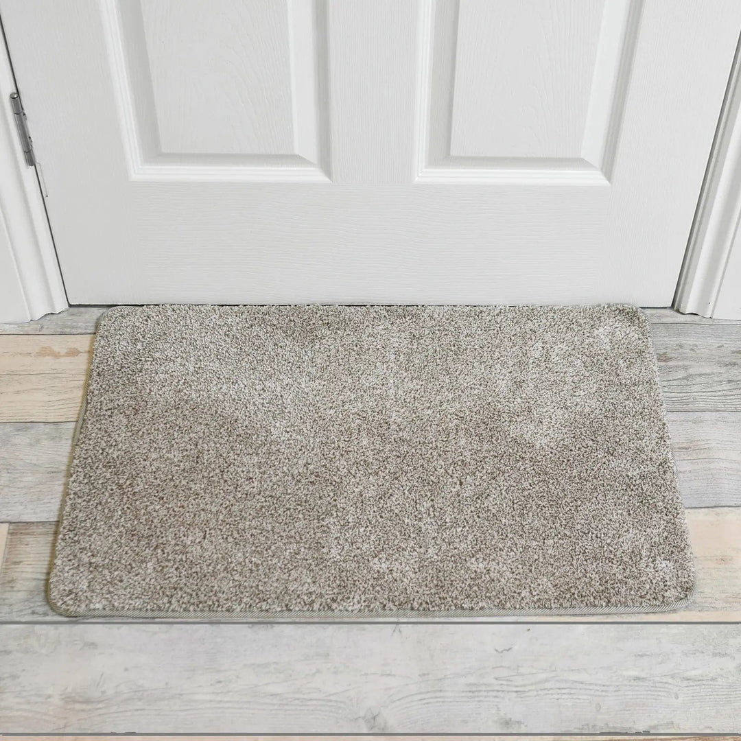 Beige door mat in front of a white wood panel door with a hardwood floor