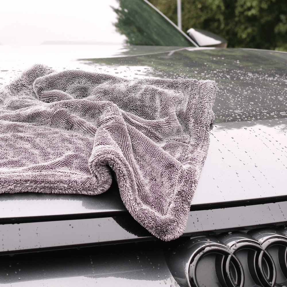 Grey microfibre towel draped over a car's bonnet with water droplets on the surface.