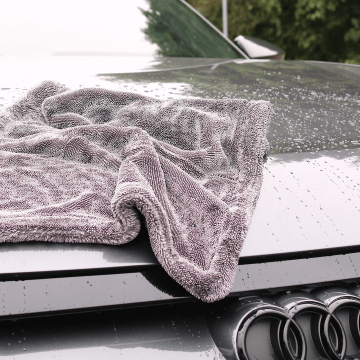 Grey microfibre towel draped over a car's bonnet with water droplets on the surface.
