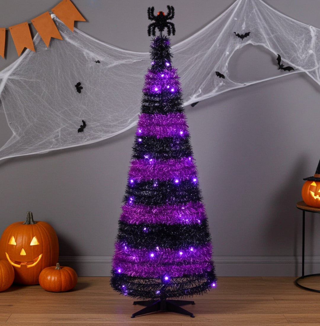 Halloween-themed tree with purple and black lights, pumpkins, and spider decorations on a gray wall.