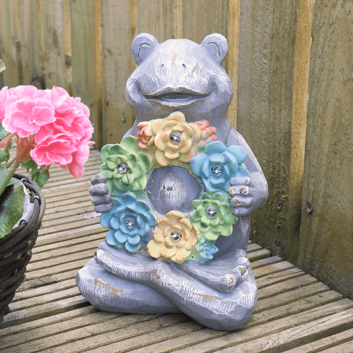 frog solar ornament on patio space beside pink flowers