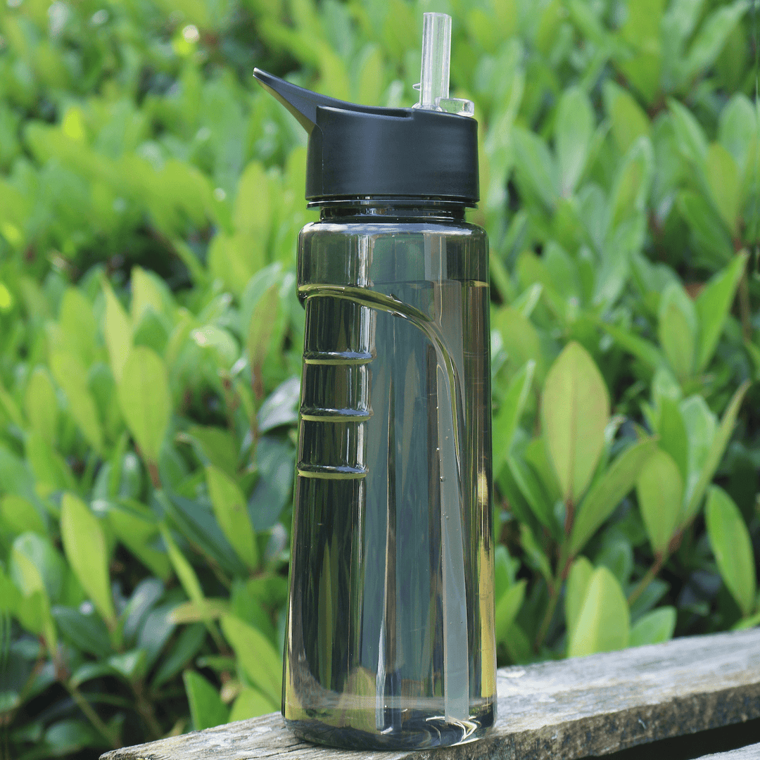 black tritan water bottle on wooden table top outdoor location, in front of foliage, filled to top with water