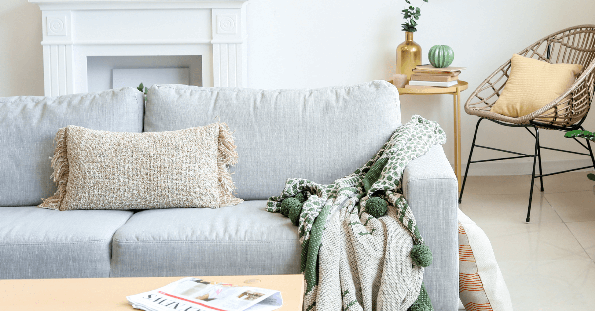 living room space featuring grey sofa, blanket throw, accent chair, cushions and side table with gold coloured vase and flower display