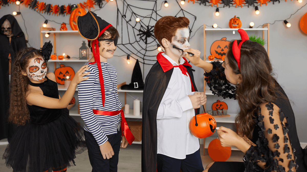 young boy at halloween party getting his face painted with white and black face paint with little boy and girl behind him watching