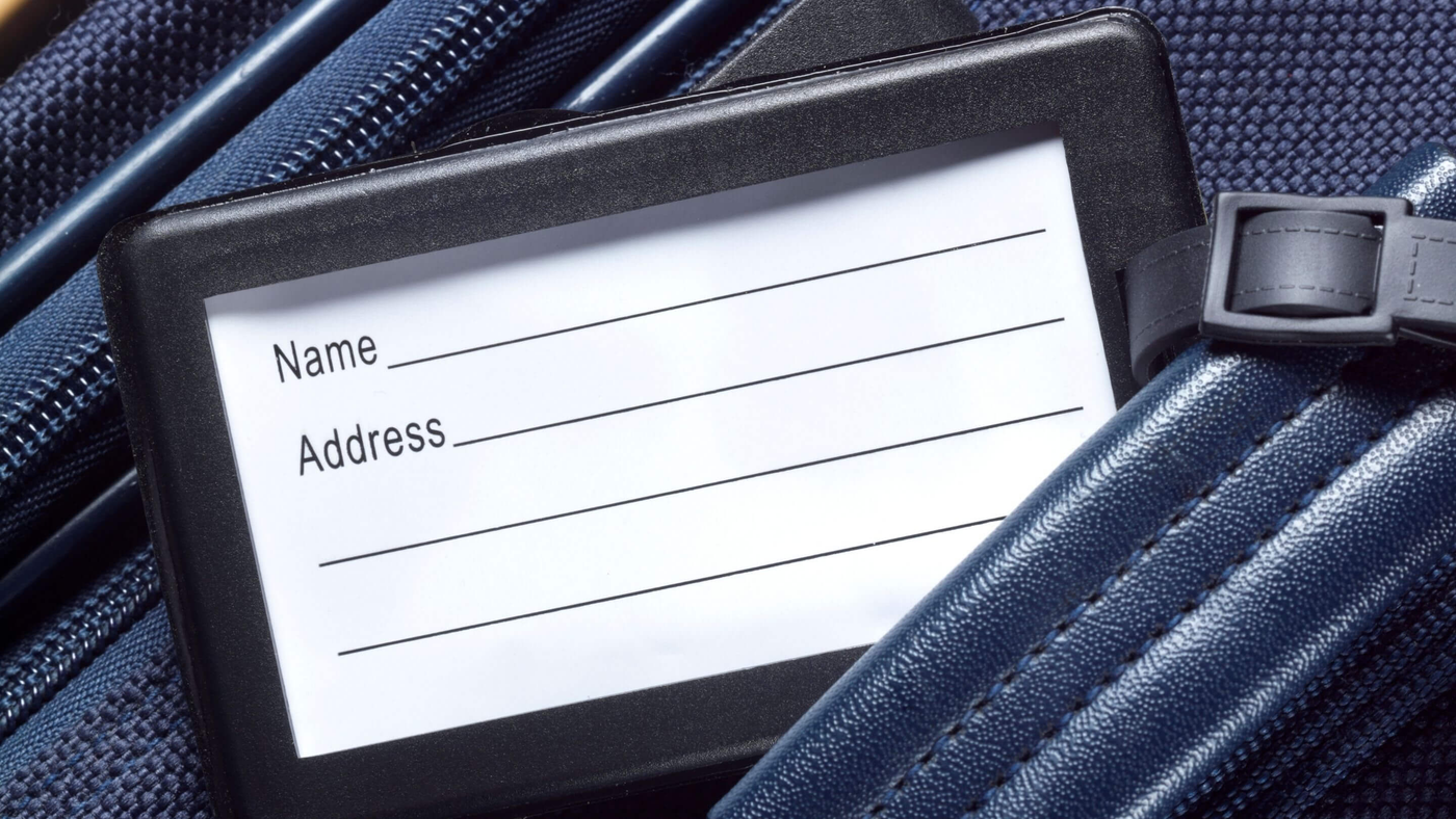 close up of luggage tag with name and address slots on top of navy blue suitcase
