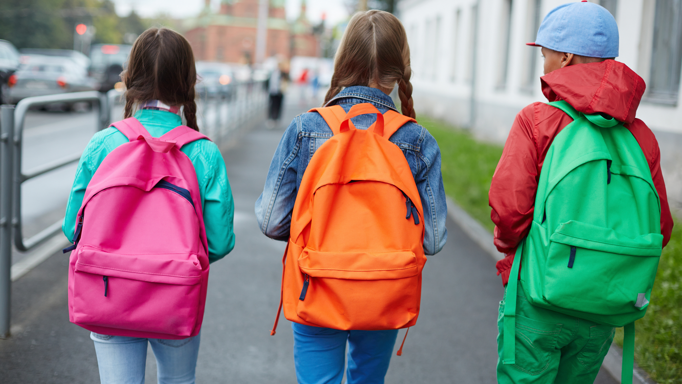 three kids walking to school with coloured backpacks on their backs