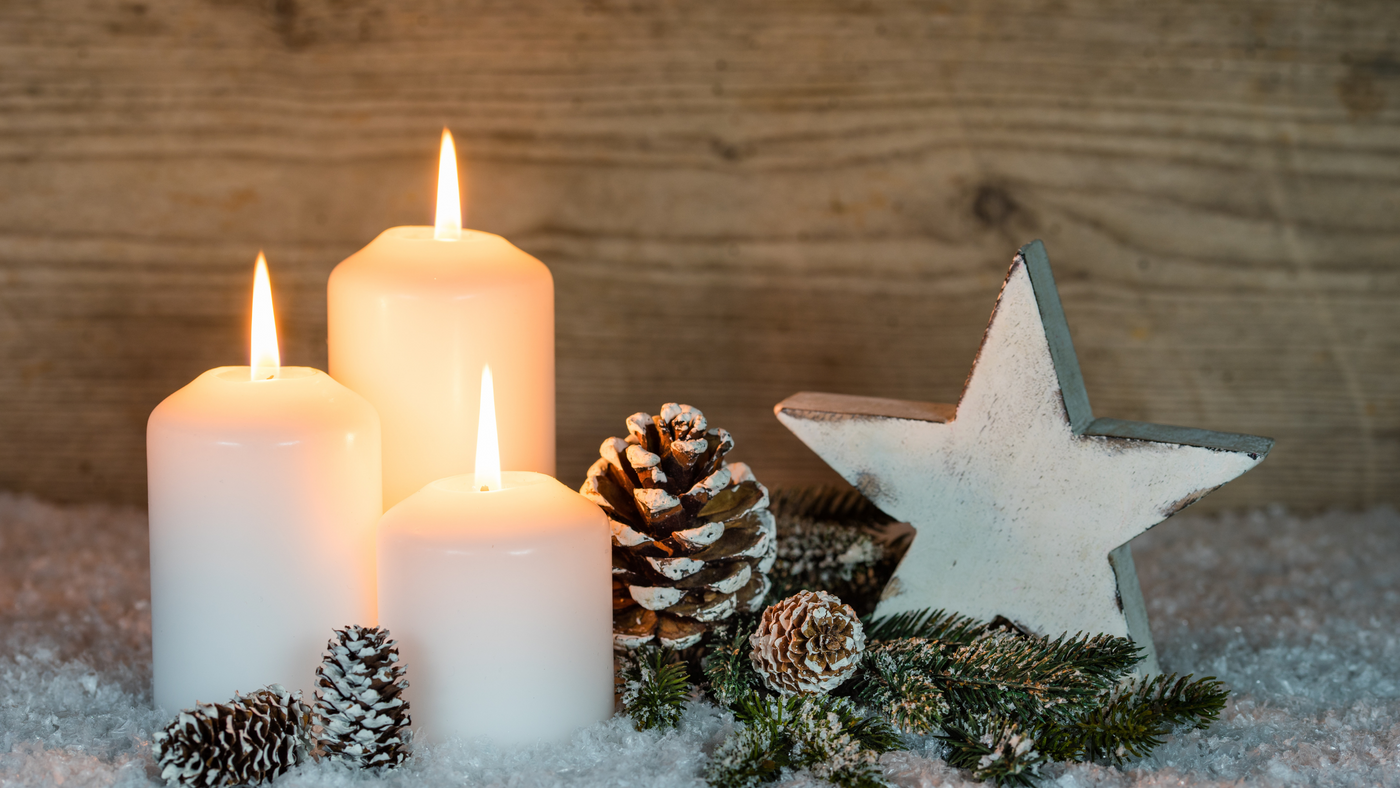 three white pillar candles beside pine cones and wooden festive star