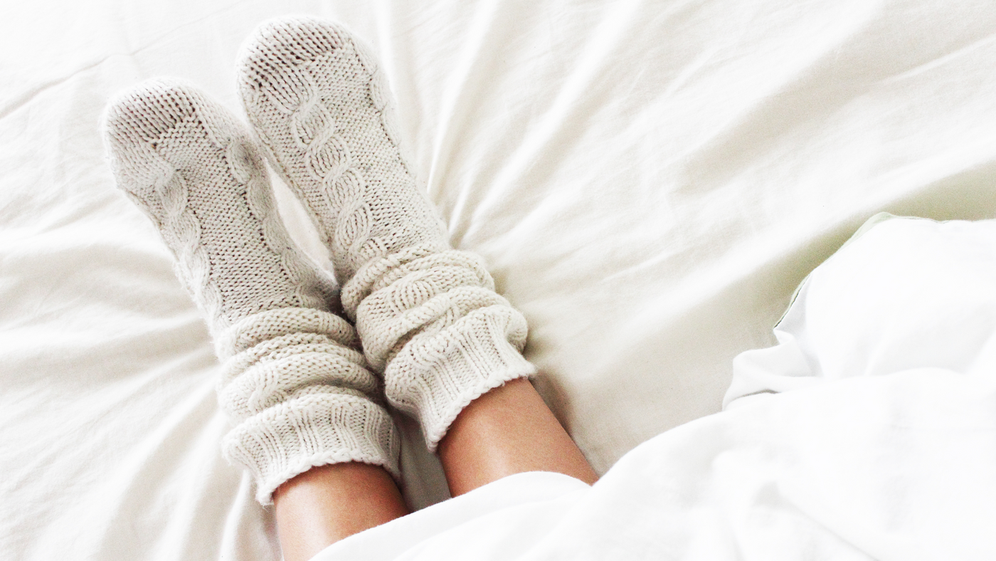 person in bed wearing cream plush slipper socks