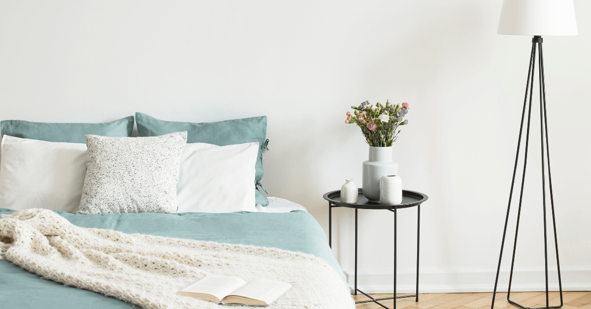 metal black side table beside large blue coloured bed with vase filled with flowers resting on top
