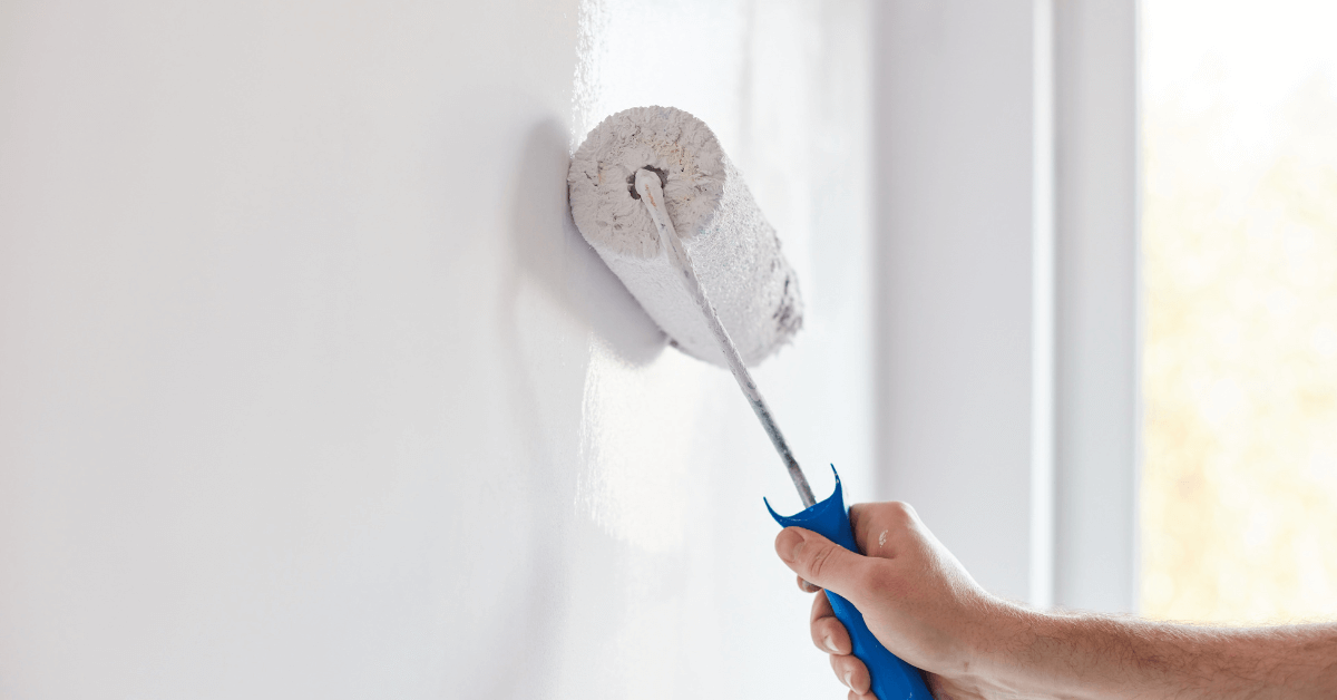 paint roller against white wall held by unidentified hand