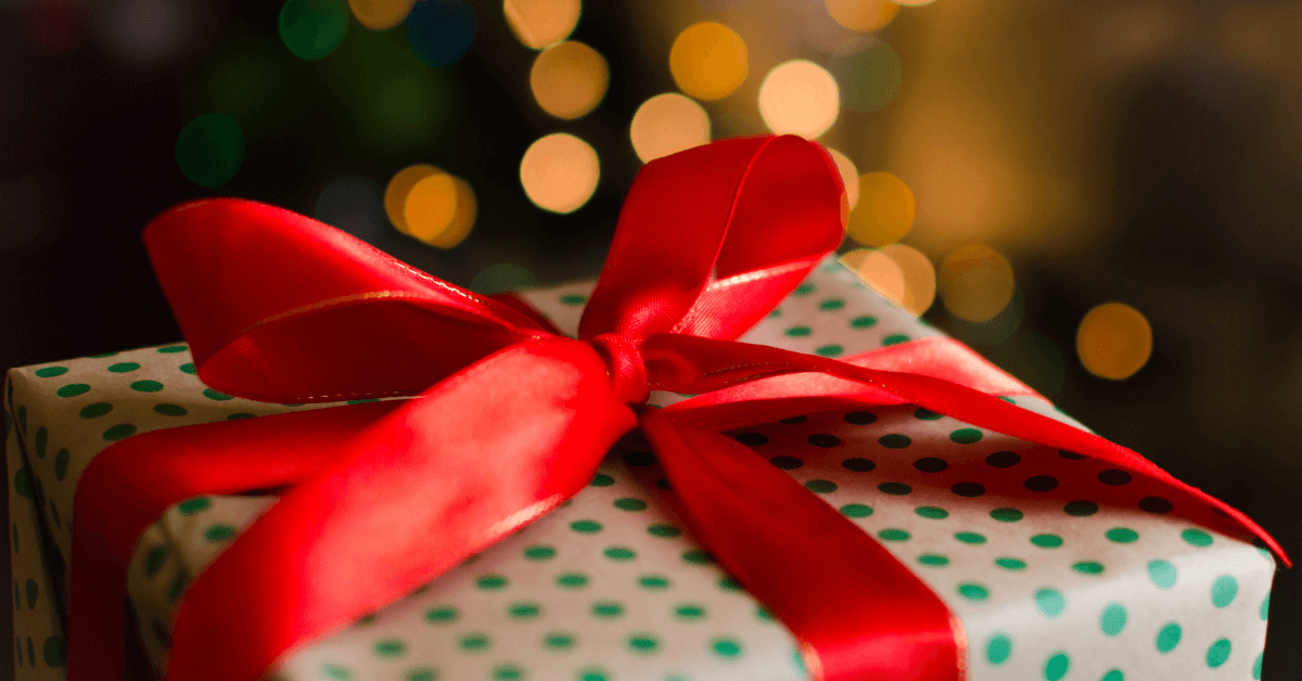 red christmas bow on polka dot wrapped christmas gift on front of christmas tree