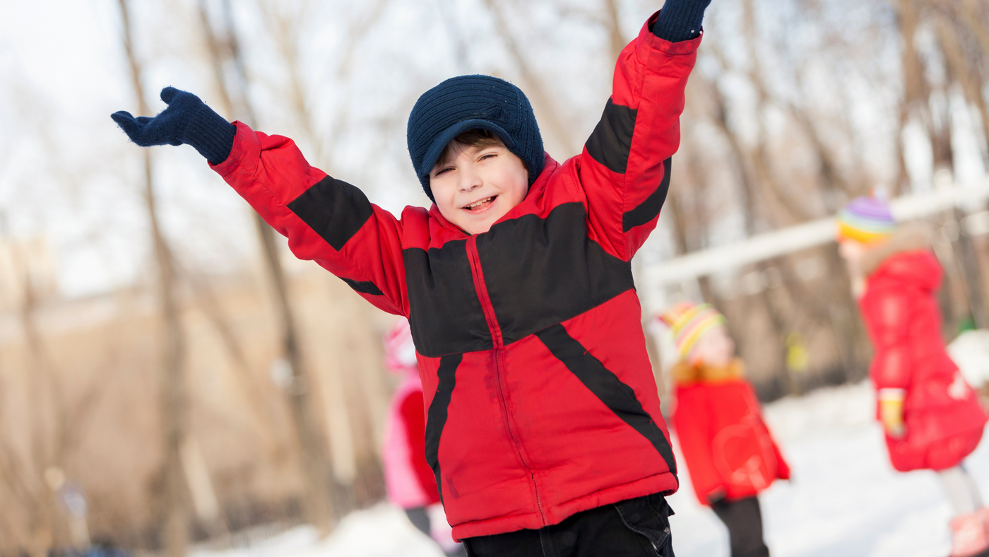 little boy in snow playing with friends wearing red jacket and navy blue hat and glove set