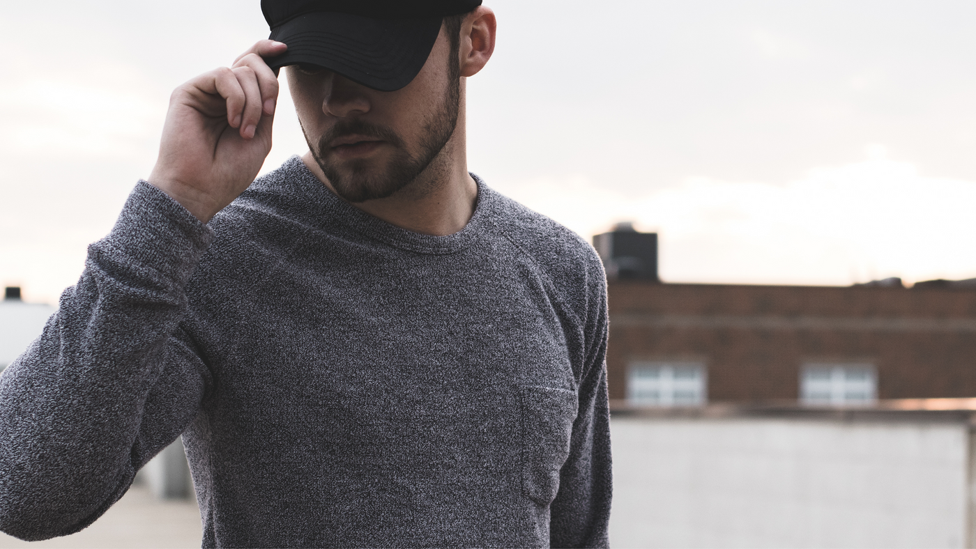 man outdoors wearing grey jumper with black cap