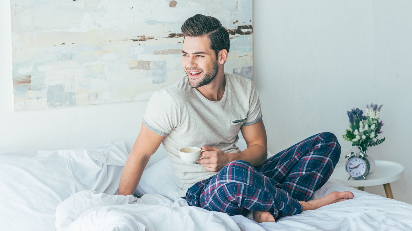 man on bed wearing striped pyjamas with a coffee mug