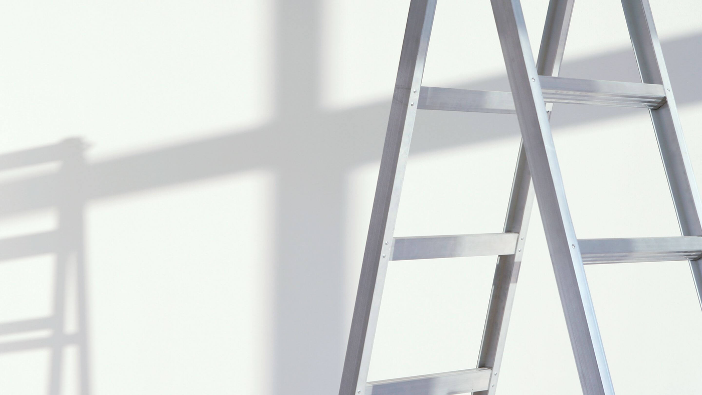 close up of silver ladder with shadows reflected on a white wall