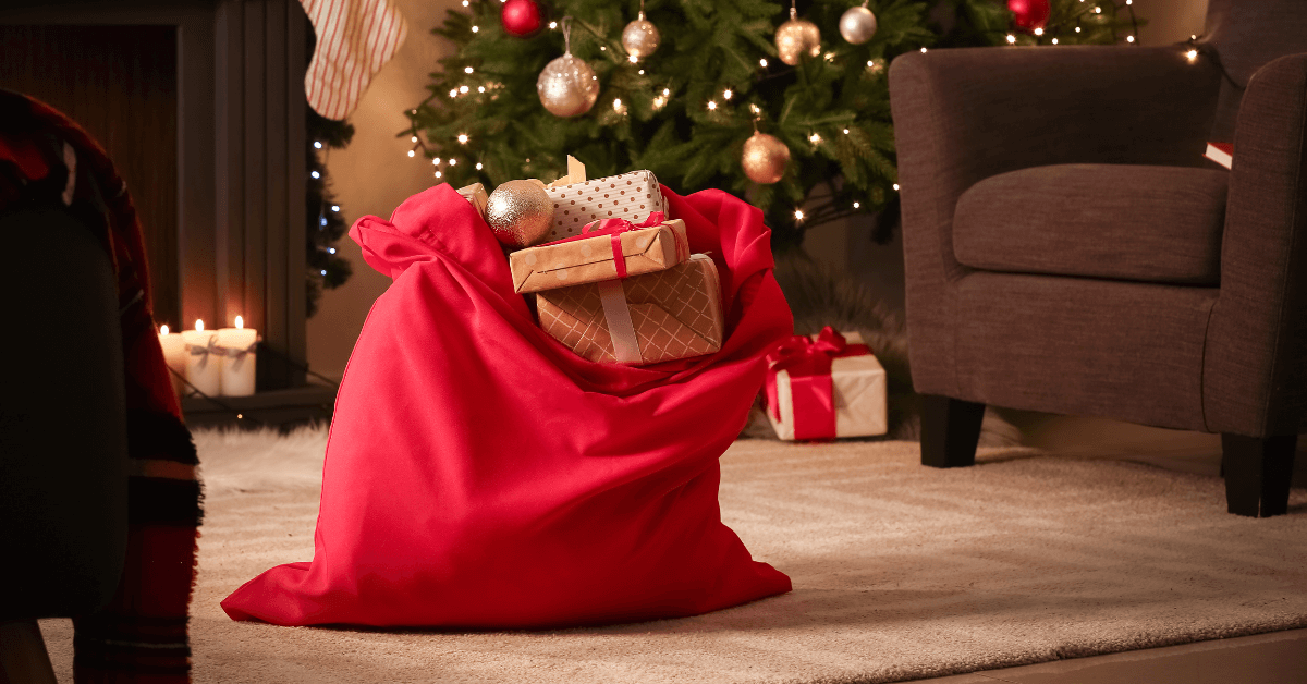 a red sack filled with christmas gifts in living room in front of christmas tree with gold and red baubles